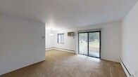 Located at 1185 Palmer Ln in East Lansing, Michigan, this 2-bedroom, 1-bathroom unit offers a practical and well-organized single-floor layout. The carpeted living room is bright and open, featuring a wall-mounted HVAC unit, baseboard heating, and a full-width sliding glass door dressed with vertical blinds that opens to a view of lush greenery — bringing in generous natural light and a pleasant outdoor connection. Adjacent to the living area, the dedicated dining room is highlighted by a pendant light fixture and a large window, with direct access to the kitchen. The kitchen features warm wood-toned cabinetry, a double-basin stainless steel sink, tile flooring, and white appliances including a refrigerator and dishwasher. The spacious primary bedroom includes a ceiling fan, natural light from a window with vertical blinds, baseboard heating, and ample closet storage with built-in hanging rods. The second bedroom also features a ceiling fan and carpeted floors. Both bedrooms are served by a full bathroom with a tub/shower combination, white tile flooring, and a vanity. Throughout the unit, clean white walls and neutral tones create a simple, functional living environment.