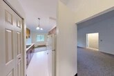 Located at 5921 Griffin Dr in Cicero, NY, this one-bedroom, one-bathroom unit offers a functional and efficient single-floor layout. The entrance opens into a hallway that connects the key living areas seamlessly. The galley-style kitchen is well-appointed with warm wood cabinetry lining both walls, white appliances including an electric range and refrigerator, a stainless steel sink, and a chandelier overhead that adds a touch of character. The kitchen flows into a combined dining and living area, where vaulted ceilings create a sense of openness. The living room features plush carpeting, a wall-mounted mini-split unit for climate control, a baseboard heater, and multiple windows that fill the space with natural light and offer views of the surrounding greenery. The bedroom is a comfortable, carpeted retreat with a window overlooking the outdoors and a baseboard heater. The bathroom is clean and straightforward, featuring a full tub-shower combo with chrome fixtures and grab bars. Three closets provide ample storage throughout the unit, and a private balcony with a distinctive blue door offers an outdoor escape. The overall ambiance is bright, clean, and practical.