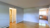This single-floor space presents a straightforward and functional interior design. The main room is finished with light-toned hardwood flooring that runs throughout, lending warmth and a sense of continuity to the space. The walls are painted in a soft, neutral gray, creating a calm and versatile backdrop suitable for a variety of furnishing styles and décor preferences. White baseboards provide a clean contrast against the flooring and walls, contributing to a crisp, well-maintained appearance.

The room is open and uncluttered, offering ample flexibility for furniture arrangement. A doorway with a classic white paneled door is visible, leading to an adjacent area, suggesting a connected layout between rooms. The ceiling is smooth and white, fitted with a simple flush-mount light fixture that keeps the look understated and practical. Electrical outlets are positioned along the walls at standard intervals, indicating readiness for immediate use.

The overall ambiance of the space is neutral and move-in ready, with clean finishes throughout. The light hardwood floors and pale gray walls combine to create a bright, airy feel, making the space feel open and easy to personalize.