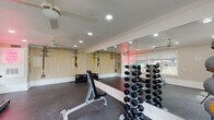 This dedicated fitness center is thoughtfully designed to support a full range of workout activities within a bright, welcoming environment. The space features durable rubber flooring throughout, providing a safe and comfortable surface for both cardio and strength training exercises. Recessed lighting and dual ceiling fans keep the room well-lit and well-ventilated, contributing to a comfortable workout atmosphere.

The strength training area is well-stocked with a tiered dumbbell rack offering a comprehensive range of weights, adjustable weight benches, and a selection of medicine balls with a dedicated storage rack. A wall-mounted TRX suspension training system provides versatility for functional fitness routines, while plyo boxes add options for high-intensity interval training.

A treadmill is positioned along the windowed wall, allowing users to enjoy outdoor views of the surrounding grounds during cardio sessions. Large windows fitted with blinds flood the space with natural light, enhancing the open and energetic feel of the room. Floor-to-ceiling mirrors span one full wall, visually expanding the space and allowing users to monitor their form during workouts.

The fitness center includes double French doors that open directly to the outdoor grounds, providing convenient access and promoting airflow. A motivational neon sign adds a playful, modern touch to the overall aesthetic of the space.