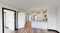 This well-appointed single-floor unit offers a clean, contemporary design with a thoughtful layout and quality finishes throughout. The open-concept kitchen serves as a central highlight, featuring crisp white shaker-style cabinetry, light granite countertops, a peninsula island with an undermount sink, and a full suite of stainless steel appliances including a refrigerator, electric range, and over-the-range microwave. Pendant lighting above the island adds a stylish touch, complemented by recessed lighting throughout the space. Durable wood-look plank flooring extends through the kitchen and main living areas, providing both practicality and visual warmth.

A hallway lined with white panel doors accented by bold black door frames connects the living area to multiple bedrooms, creating a striking design contrast. One bedroom features plush carpet and a large sliding glass door with vertical blinds, offering access to an outdoor balcony and bringing in natural light. Another bedroom is finished with wood-look plank flooring, a window with outdoor views, and a built-in storage unit. The primary suite includes a full bathroom with a soaking tub, white vanity, and wood-look flooring, as well as a spacious walk-in closet with built-in shelving. The unit's neutral palette and modern finishes create a cohesive, move-in ready atmosphere throughout.