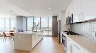 Located at 100 Park Ave in Fort Lee, NJ, this thoughtfully designed one-bedroom, one-bathroom residence offers a refined modern living experience with stunning panoramic views. Floor-to-ceiling windows run throughout the unit, flooding every room with natural light and framing expansive vistas of the surrounding skyline and landscape.

The open-concept kitchen, dining, and living area serves as the heart of the home. The kitchen is outfitted with sleek white cabinetry, a light stone countertop island, stainless steel appliances including a gas range, built-in microwave, and French door refrigerator, and a subtle grey subway tile backsplash. Light hardwood flooring flows seamlessly across the entire living space, complementing the clean, contemporary palette. The dining area accommodates an intimate seating arrangement set against a backdrop of dramatic floor-to-ceiling glass. The living room features soaring ceilings and continues the floor-to-ceiling window theme, offering exceptional light and views.

The bedroom is a comfortable retreat with large windows, ample natural light, and generous proportions. A dedicated walk-in closet provides excellent storage with built-in shelving and hanging rods. The bathroom is finished with large-format tile, a dark wood vanity, and modern wall-mounted lighting. The overall ambiance is clean, luminous, and contemporary throughout.