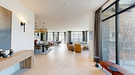 Located at 110 Addison Rd in Athens, Georgia, this thoughtfully designed single-floor amenity space offers residents a sophisticated setting for socializing, dining, and recreation. The open-plan layout is anchored by striking herringbone-patterned light wood flooring that flows seamlessly throughout the main gathering areas, creating a warm and cohesive aesthetic.

The expansive social lounge features multiple seating arrangements, including plush sofas and accent chairs, all bathed in abundant natural light from dramatic floor-to-ceiling steel-framed windows that frame views of the surrounding community. A corner sitting nook with wraparound glazing provides an intimate retreat within the larger space.

The gourmet kitchen is outfitted with deep green cabinetry, a large white quartz island with brass fixtures, and professional-grade appliances, opening directly to a formal dining area appointed with a dark wood table, velvet upholstered chairs, tiered rattan chandeliers, and a curated gallery wall of framed black-and-white photography.

A dedicated game room includes a full-size shuffleboard table, pool table, and high-top seating, while a lounge area with textured wallcovering and leather barrel chairs offers a more relaxed retreat. Exterior access points connect the interior to outdoor terrace areas, enhancing the overall sense of openness and connectivity.