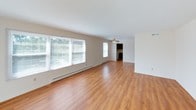 This single-floor, three-bedroom, two-bathroom residence offers a well-organized and functional layout spanning a comfortable living footprint. The entry greets you with a clean, well-lit hallway featuring warm hardwood-style flooring that continues through the main living areas. The expansive living room is bright and open, with large windows along one wall allowing generous natural light to fill the space, complemented by a ceiling fan and baseboard heating. A sliding glass door leads to an outdoor view, further enhancing the airy feel of the room. The kitchen features dark wood cabinetry providing ample storage, light countertops, a double stainless steel sink, and white appliances including a range and refrigerator, all set on hardwood-style flooring beneath a drop ceiling. The bedrooms are carpeted and well-proportioned, each offering natural light through multiple windows and baseboard heating. Notably, the bedrooms provide exceptional closet storage, with some rooms featuring multiple built-in closets with dedicated hanging rods. The two bathrooms are tiled and functional, each equipped with a tub-shower combination, vanity cabinetry, and ventilation. Overall, the residence presents a practical and comfortable living environment with consistent finishes throughout.