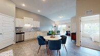 This single-floor unit is designed with an open-concept layout that seamlessly connects the kitchen, dining, and living areas. The kitchen is well-appointed with white shaker-style cabinetry, granite countertops, stainless steel appliances including a range, microwave, dishwasher, and refrigerator, and a deep sink. The vaulted ceilings in the main living area add a sense of openness and volume, while large sliding doors allow natural light to pour in and provide direct access to a private balcony with outdoor views.

The dining area accommodates a round table with ample space, positioned between the kitchen and the living room, which features a cozy seating nook with additional storage. Durable tile-style flooring runs throughout the main living spaces, offering both practicality and a clean aesthetic.

The bedroom is carpeted for comfort and includes a closet and a window that brings in natural light. The bathroom features a white vanity with storage, tile flooring, and a clean, minimalist design. A dedicated in-unit laundry area houses a full-sized washer and dryer with overhead wire shelving for added storage convenience. The overall ambiance is modern, bright, and functional.