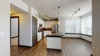 This single-floor residence showcases a contemporary design with a cohesive mix of finishes throughout. The open-concept kitchen serves as a central highlight, featuring white cabinetry extending to the ceiling, a dark granite-topped island with an integrated sink, and stainless steel appliances including a French door refrigerator, range, and microwave. A rich, dark tile backsplash adds contrast, while a combination of pendant lighting and track lighting illuminates the space. Wood-look luxury vinyl plank flooring extends through the kitchen and living areas, complemented by large windows that draw in natural light.

The bedrooms offer plush carpeting, ceiling fans, and windows with horizontal blinds. One room features a wall of windows providing additional natural light and views, while another carpeted room includes a utility panel, offering flexible use.

Two bathrooms serve the unit. The primary bath includes large-format gray tile flooring, a soaking tub, a glass-enclosed shower with tile surround, and a long white vanity with dark countertops and dual sinks. The secondary bath features a white vanity with dark countertops, a framed mirror, and tile flooring, maintaining the same modern aesthetic throughout.