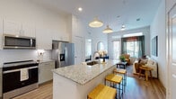 This single-floor residence showcases a thoughtfully designed open-concept layout with a cohesive, modern aesthetic throughout. The kitchen serves as a central highlight, featuring granite countertops, white shaker-style cabinetry extending to the ceiling, a textured tile backsplash, and a full suite of stainless steel appliances. A spacious island with an undermount sink and seating provides both functionality and a natural gathering point, illuminated by statement pendant lights overhead. The kitchen flows seamlessly into the living area, where large windows and a glass door admit generous natural light and offer outdoor views. The living room provides a comfortable, well-proportioned space with room for a full seating arrangement.

The two bedrooms are bright and tranquil, each featuring large windows and neutral walls. One bedroom includes an en-suite bathroom equipped with a granite-topped vanity with an illuminated mirror, a soaking tub, and a separate glass-enclosed walk-in shower with white tile surround. The second bathroom mirrors the same refined finishes. Light wood-look flooring runs consistently throughout the main living areas, lending warmth and visual continuity to the overall design.