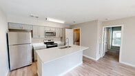 Located at 1620 Bay Area Blvd in Houston, TX, this one-bedroom, one-bathroom unit offers a well-designed layout that maximizes every square foot of its compact footprint. The kitchen serves as a central hub of the home, featuring a large island with a white quartz countertop and an integrated sink, gray shaker-style cabinetry, light wood-look flooring, and a full suite of stainless steel appliances including a refrigerator, range, and microwave. The open design allows the kitchen to connect seamlessly to the living area. The bedroom is a comfortable retreat, finished with plush carpeting, a ceiling fan with light fixture, and a window that brings in natural light. It provides direct access to both the bathroom and a dedicated closet area. The bathroom is clean and modern, showcasing a white quartz vanity top, an undermount sink with a brushed nickel faucet, gray cabinetry, and a large frameless wall mirror. A separate laundry area accommodates a stacked washer and dryer unit alongside additional shelving. The unit also features a private outdoor balcony enclosed by a horizontal wood-slat railing, offering views of the surrounding community. Neutral tones and consistent finishes give the space a cohesive, move-in-ready feel throughout.