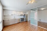 Located at 521 2nd Ave W in Seattle's desirable Queen Anne neighborhood, this thoughtfully designed one-bedroom, one-bathroom apartment offers a smart and efficient layout. The open-concept kitchen and living area serves as the heart of the space, featuring warm hardwood-style flooring, recessed lighting, and a ceiling fan. The kitchen is outfitted with crisp white upper cabinetry, wood-toned lower cabinets, light quartz countertops, and a full suite of stainless steel appliances including a refrigerator, range, and dishwasher. A striking frosted glass sliding partition elegantly separates the living area from the bedroom, allowing natural light to filter through while maintaining privacy. The bedroom is compact yet functional, with a large window offering views of the surrounding urban streetscape. A well-organized hallway connects the living spaces to three closets, providing ample storage throughout. The bathroom is spacious and accessibility-friendly, featuring safety grab bars, a wood-toned vanity, and durable vinyl tile flooring. Clean white walls and consistent hardwood-style flooring throughout the unit create a cohesive, modern aesthetic that feels bright and welcoming.