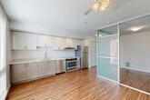 Located at 521 2nd Ave W in Seattle's desirable Queen Anne neighborhood, this thoughtfully designed one-bedroom, one-bathroom apartment offers a smart and efficient layout. The open-concept kitchen and living area serves as the heart of the space, featuring warm hardwood-style flooring, recessed lighting, and a ceiling fan. The kitchen is outfitted with crisp white upper cabinetry, wood-toned lower cabinets, light quartz countertops, and a full suite of stainless steel appliances including a refrigerator, range, and dishwasher. A striking frosted glass sliding partition elegantly separates the living area from the bedroom, allowing natural light to filter through while maintaining privacy. The bedroom is compact yet functional, with a large window offering views of the surrounding urban streetscape. A well-organized hallway connects the living spaces to three closets, providing ample storage throughout. The bathroom is spacious and accessibility-friendly, featuring safety grab bars, a wood-toned vanity, and durable vinyl tile flooring. Clean white walls and consistent hardwood-style flooring throughout the unit create a cohesive, modern aesthetic that feels bright and welcoming.