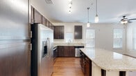 Located at 2020 Proximity Dr in Charleston, SC, this well-appointed one-bedroom, one-bathroom unit offers a smart and functional single-floor layout. The open-concept kitchen and living area serves as the heart of the home, showcasing rich dark-espresso cabinetry, light granite countertops, and a full suite of stainless steel appliances including a French door refrigerator, range, microwave, and dishwasher. A peninsula island with seating provides additional prep and dining space, while stylish pendant lighting and a track light fixture lend a modern touch. Warm hardwood-style flooring flows consistently throughout the unit, creating a cohesive and inviting atmosphere. The bedroom is generously proportioned, featuring multiple windows with blinds that allow ample natural light, and is equipped with a ceiling fan for year-round comfort. A spacious walk-in closet with wire shelving offers practical storage. The full bathroom includes a tiled tub/shower combination, tile flooring, and a dark-wood vanity. A dedicated laundry room houses a full-size washer and dryer with additional wire shelving. Neutral wall tones and clean finishes throughout give this unit a bright, move-in-ready appeal.