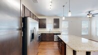 Located at 2020 Proximity Dr in Charleston, SC, this well-appointed one-bedroom, one-bathroom unit offers a smart and functional single-floor layout. The open-concept kitchen and living area serves as the heart of the home, showcasing rich dark-espresso cabinetry, light granite countertops, and a full suite of stainless steel appliances including a French door refrigerator, range, microwave, and dishwasher. A peninsula island with seating provides additional prep and dining space, while stylish pendant lighting and a track light fixture lend a modern touch. Warm hardwood-style flooring flows consistently throughout the unit, creating a cohesive and inviting atmosphere. The bedroom is generously proportioned, featuring multiple windows with blinds that allow ample natural light, and is equipped with a ceiling fan for year-round comfort. A spacious walk-in closet with wire shelving offers practical storage. The full bathroom includes a tiled tub/shower combination, tile flooring, and a dark-wood vanity. A dedicated laundry room houses a full-size washer and dryer with additional wire shelving. Neutral wall tones and clean finishes throughout give this unit a bright, move-in-ready appeal.