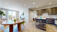 This single-floor residence is thoughtfully designed with an open-concept layout that seamlessly connects the kitchen, dining, and living areas. Light hardwood-style flooring flows throughout, complementing the neutral gray and white color palette that gives the space a clean, contemporary feel. Recessed lighting illuminates each room, enhancing the bright, airy atmosphere.

The kitchen is a functional centerpiece, featuring dark walnut-toned cabinetry extending to the ceiling, white countertops, and a full suite of stainless steel appliances including a gas range, microwave, dishwasher, and French door refrigerator. A freestanding island with bar seating provides additional prep space and casual dining options.

The dining area accommodates a round wood table paired with vibrant green modern chairs, while the adjacent living room benefits from abundant natural light pouring through a sliding glass door that opens to a private balcony offering panoramic outdoor views.

The bedroom is serene and well-proportioned, featuring large windows framing scenic views, hardwood-style flooring, and access to a spacious walk-in closet with wire shelving. The bathroom includes a dark wood vanity, white countertop, built-in shelving, and a tub-shower combination.