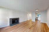 Located at 13846 NE 8th St in Bellevue, WA, this 2-bedroom, 1-bathroom residence offers a well-organized single-level layout that makes efficient use of its space. A welcoming hallway with warm hardwood flooring leads into an open living area anchored by a classic stone-surround fireplace with a white mantle, creating a cozy focal point. Sliding glass doors allow natural light to fill the living space and provide views of the surrounding greenery. The kitchen is thoughtfully designed in a U-shape configuration, featuring white shaker cabinetry, light countertops, stainless steel appliances including a dishwasher, range, microwave, and refrigerator, along with a window overlooking the outdoors. The primary bedroom is generously sized, with a curved bay window framing lush outdoor views and ample natural light. The second bedroom also benefits from a window with garden views and includes a sliding-door closet. Both bedrooms feature the same warm hardwood flooring found throughout the home. The bathroom offers a full tub-shower combination. Clean white walls and consistent flooring throughout give the home a bright, cohesive feel that is both functional and inviting.