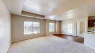 Located at 2100 Spencer Rd in Denton, TX, this single-story home offers a functional and comfortable layout with two bedrooms and two bathrooms. The open-concept living room is bright and welcoming, featuring plush carpet, a textured ceiling with a tray detail, and multiple windows dressed with blinds that allow generous natural light and views of the surrounding neighborhood. A private entry door with glass paneling adds to the airy feel of the main living area, which transitions to warm hardwood-style flooring near the entryway.

The kitchen is well-appointed with rich dark wood cabinetry, light-toned countertops, hardwood-style flooring, and white appliances including an electric range and refrigerator. A peninsula with a built-in sink provides added workspace and storage.

The primary bedroom features a tray ceiling, a ceiling fan, carpet flooring, two windows for ample natural light, a private en-suite bathroom, and a dedicated walk-in closet. The second bedroom is similarly carpeted with a tray ceiling detail, a window with outdoor views, and its own closet access.

Both bathrooms include dark wood cabinetry, light countertops, hardwood-style flooring, and a tub-shower combination with tiled surrounds, offering a clean and practical design throughout.