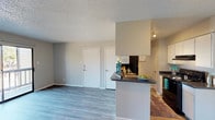 This single-story apartment at The Summit Apartments offers a thoughtfully designed open-concept layout that seamlessly connects the main living areas. The living room is a welcoming space featuring wood-style laminate flooring, neutral gray walls, and a textured ceiling. A sliding glass door fills the room with natural light and opens directly onto a private balcony, providing outdoor views and additional ventilation.

The galley-style kitchen is efficiently arranged with white cabinetry, dark granite-style countertops, and black appliances including a refrigerator, electric range, and dishwasher. A peninsula counter separates the kitchen from the living and dining areas, offering additional prep space and a casual bar-style seating option. Track lighting overhead ensures the kitchen is well-illuminated.

The bedroom is carpeted for comfort and includes a ceiling fan with light fixture, a window with blinds for natural light, a walk-in closet, and direct access to the bathroom. The bathroom features a dark granite-style vanity countertop, a large mirror with overhead lighting, white cabinetry, and a shower-tub combination. Additional storage is available through the closets visible throughout the unit.