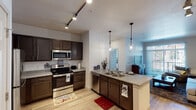 This single-floor residence offers a thoughtfully designed layout that connects the kitchen, living area, bedroom, and bathroom in a functional flow. The kitchen is a standout feature, outfitted with rich dark-brown cabinetry, granite-style countertops, and a full suite of stainless steel appliances including a refrigerator, electric range, microwave, and dishwasher. Light wood-style flooring runs throughout, and track lighting overhead ensures bright, even illumination. A peninsula with a double sink and pendant lighting above adds both workspace and visual interest, opening naturally toward the dining and living areas. The living room is bright and comfortable, featuring a sliding glass door with vertical blinds that provides access to a private balcony and invites natural light into the space. The bedroom offers plush carpeting, a ceiling fan, and dual windows that bring in additional daylight and exterior views. The bathroom includes a combined shower and tub enclosure with white tile surround, offering a clean and practical finish. Overall, the space presents a modern, cohesive aesthetic suited for comfortable everyday living.