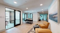 Located at 700 SE Veranda Pl in Port Saint Lucie, Florida, this single-floor amenity space offers a thoughtfully designed layout that balances comfort, function, and contemporary style. The space is divided into distinct yet cohesive areas, including two living rooms and two dining rooms, each with its own character and purpose.

One living area features warm light wood flooring, recessed lighting, and a pair of mustard-yellow lounge chairs arranged around a sculptural coffee table, complemented by a large coastal landscape painting. Adjacent to this is a lounge nook with vibrant teal carpeting, floor-to-ceiling windows, and views of palm trees — perfect for casual gatherings or focused work.

The dining areas are equally refined. One features a solid natural wood conference table surrounded by upholstered chairs, illuminated by a striking brass pendant light with globe fixtures, and accented by sculptural white wall art. The other dining space showcases a bold tropical-leaf accent wall with booth-style seating and pendant lighting, creating a dynamic and inviting atmosphere.

Throughout the space, a cohesive coastal palette of teal, warm neutrals, and natural wood tones ties each area together. Large windows flood the interiors with natural light and provide views of the surrounding palm-lined community.
