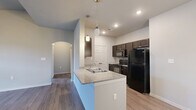 This 1-bedroom, 1-bathroom unit is thoughtfully designed to maximize functionality across a single floor. The combined kitchen and living area serves as the heart of the home, where the kitchen stands out with dark espresso cabinetry, granite-style countertops, black appliances including a refrigerator, electric range, and built-in microwave, and a peninsula island with a double sink and stylish pendant lighting overhead. Wood-style flooring runs throughout, lending a cohesive and modern aesthetic. The living area benefits from soaring vaulted ceilings, a ceiling fan, and a glass door that invites natural light, creating an open and airy atmosphere. An elegant arched doorway connects the living space to the hallway, adding a subtle architectural detail. The bedroom is a comfortable, well-proportioned retreat featuring a ceiling fan, a window with natural light, and easy access to a dedicated closet. The bathroom is clean and practical, appointed with a dark vanity, granite-style countertop, a wall mirror with lighting, and a full shower-tub combo. Additional utility and storage spaces round out the floor plan, and a spacious double-door closet is accessible from the kitchen area, adding practical convenience to this well-organized home.