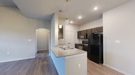 This 1-bedroom, 1-bathroom unit is thoughtfully designed to maximize functionality across a single floor. The combined kitchen and living area serves as the heart of the home, where the kitchen stands out with dark espresso cabinetry, granite-style countertops, black appliances including a refrigerator, electric range, and built-in microwave, and a peninsula island with a double sink and stylish pendant lighting overhead. Wood-style flooring runs throughout, lending a cohesive and modern aesthetic. The living area benefits from soaring vaulted ceilings, a ceiling fan, and a glass door that invites natural light, creating an open and airy atmosphere. An elegant arched doorway connects the living space to the hallway, adding a subtle architectural detail. The bedroom is a comfortable, well-proportioned retreat featuring a ceiling fan, a window with natural light, and easy access to a dedicated closet. The bathroom is clean and practical, appointed with a dark vanity, granite-style countertop, a wall mirror with lighting, and a full shower-tub combo. Additional utility and storage spaces round out the floor plan, and a spacious double-door closet is accessible from the kitchen area, adding practical convenience to this well-organized home.