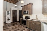 This single-floor loft-style unit showcases a compelling blend of industrial character and contemporary design. Soaring ceilings with exposed wooden beams and open rafters lend a raw, architectural warmth throughout the living areas, while large windows flood the space with generous natural light, casting bright patterns across the floors.

The kitchen is a standout feature, outfitted with rich, dark-stained shaker-style cabinetry, granite countertops, and a classic white subway tile backsplash. Stainless steel appliances — including a range, microwave, dishwasher, and refrigerator — complement the space's modern sensibility, while pendant lights hang from the exposed beam ceiling above, adding an industrial-chic touch. Wood-look plank flooring runs throughout the kitchen and main living areas, enhancing the loft aesthetic.

The bedrooms offer a quieter atmosphere, carpeted for comfort, with large windows that bring in abundant daylight and ceiling fans overhead. The exposed brick and open rafter details visible in these rooms reinforce the building's industrial heritage.

Both bathrooms are cleanly finished with walk-in showers featuring white surrounds, granite-topped vanities with dark wood cabinetry, and wood-look flooring. One bathroom also includes built-in open shelving for added storage. The overall ambiance is modern and refined, with nods to the building's historic industrial roots at every turn.