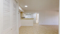 Located at 7050 Northwest 179th Street in Hialeah, FL, this single-floor, 3-bedroom, 1-bathroom home offers a clean and functional layout finished with light beige ceramic tile flooring throughout. The open-concept living and kitchen area forms the heart of the home, where the kitchen features a peninsula counter with a decorative mosaic tile trim, white cabinetry, a tile backsplash in warm earth tones, and white appliances including a range and refrigerator. The living area is bright and spacious, with a sliding glass door that opens to a balcony overlooking lush palm trees and the surrounding neighborhood streetscape. Each of the three bedrooms is finished with the same neutral tile flooring and features windows that bring in natural light and views of the tropical greenery outside. Two closets provide dedicated storage within the unit. The bathroom is appointed with a full soaking tub and a striking marble-look tile surround reaching from floor to ceiling, lending a clean and polished aesthetic. The overall design is minimal and bright, with white walls and recessed lighting creating a consistently airy atmosphere throughout the home.