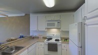 This single-floor residence offers a practical and well-appointed layout designed for comfortable everyday living. The kitchen serves as a central highlight of the space, showcasing crisp white cabinetry that extends from floor to ceiling, providing generous storage throughout. The cabinetry is complemented by light-toned countertops that offer ample workspace for meal preparation. Appliances include a white electric range with coil burners, an over-the-range microwave, a dishwasher, and a full-size refrigerator, creating a cohesive and fully equipped cooking environment. The kitchen is arranged in an efficient L-shaped configuration, maximizing workflow and accessibility. Overhead flush-mount lighting ensures the space is well-illuminated. The neutral color palette throughout — white cabinetry against warm-toned walls — lends the kitchen a clean, timeless aesthetic. The overall design of the residence emphasizes functionality and practicality, making it a welcoming space suited to a variety of lifestyles. The single-floor layout ensures seamless accessibility and easy navigation throughout the home.