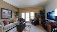 This single-floor residence offers a thoughtfully designed layout that balances comfort and functionality across its key living spaces. The living room serves as the heart of the home, featuring warm beige walls, plush carpeting, and a set of glass patio doors flanked by windows that draw in natural light and provide outdoor views. The space comfortably accommodates a full seating arrangement centered around a distinctive trunk-style coffee table atop a colorful area rug.

Adjacent to the living area, the dining room features wood-look flooring, a wooden dining table with mixed seating, and a corner display cabinet, creating an inviting space for meals. The kitchen is equipped with warm wood cabinetry, light countertops, and black appliances including a refrigerator, electric range, and built-in microwave.

The bedrooms are carpeted and well-sized, each featuring ceiling fans and windows for natural light. One bedroom showcases a bold blue accent wall, while another offers a walk-in closet with built-in shelving. Two bathrooms serve the residence—one with a walk-in shower and wood-look flooring, the other featuring a soaking tub and warm-toned vanity cabinetry, both finished with clean, neutral palettes.