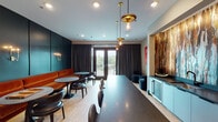 Located at 3700 National Dr in Raleigh, NC, this stylish single-floor clubroom is thoughtfully designed to serve as a sophisticated social and event space. The interior showcases a carefully curated aesthetic, blending contemporary design elements with warm, inviting accents throughout.

The lounge area features a continuous burnt-orange velvet banquette running along a deep teal accent wall, paired with marble-topped round tables and curved leather chairs. Pendant lighting with brass fixtures hangs above a large dark-surfaced communal table, creating an inviting atmosphere suited for both casual gatherings and organized events.

A well-appointed wet bar anchors one side of the room, complete with dark countertops, teal lower cabinetry, an undermount sink, and a beverage refrigerator. Above, open glass-front upper cabinets display spirits and barware, while a dramatic floor-to-ceiling abstract artwork in warm earth tones serves as a striking focal point behind the bar.

Bold curated artwork punctuates the walls throughout, complementing the space's upscale ambiance. Light wood-style flooring runs throughout, adding warmth against the darker design elements. French doors open to an outdoor balcony, offering natural light and views of the surrounding greenery, further enhancing the inviting character of this well-designed gathering space.