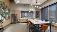 The clubroom at 434 W Lake St in Minneapolis, MN, is a thoughtfully designed communal space that blends contemporary aesthetics with functional amenities. The single-floor layout is anchored by polished concrete floors that reflect light throughout the open interior, creating a sleek, urban feel.

The kitchen and dining area is a standout feature, equipped with stainless steel appliances — including a full-size refrigerator and dishwasher — and light wood cabinetry set against a dramatic deep-blue glazed tile backsplash. A large white-topped communal table with a bold blue steel base is surrounded by warm cognac leather chairs, ideal for casual dining or collaborative gatherings. Above, an artful cluster of Edison bulbs suspended on colorful cords serves as a striking statement lighting installation.

The lounge area offers a welcoming retreat, anchored by a sleek linear fireplace set into a white tile accent wall, topped with a natural wood mantel and a wall-mounted television. Comfortable seating — including plush sofas and accent chairs — is arranged to encourage conversation, while large windows with sheer roller shades flood the space with natural light and provide views of the surrounding neighborhood.

Vibrant original artwork, textured feature walls, and carefully selected greenery add personality and warmth throughout, making this clubroom a well-rounded, inviting space for socializing and relaxation.