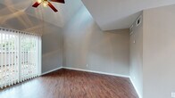 This two-story, one-bedroom, two-bathroom home offers an efficient and well-organized layout spread across two floors. The main level features a welcoming living area with striking vaulted ceilings that create an airy sense of openness, complemented by warm hardwood-style flooring and a ceiling fan with light fixture. A sliding glass door dressed with vertical blinds fills the space with natural light and provides access to the outdoors. The kitchen is efficiently laid out with warm wood cabinetry, a stainless steel refrigerator, electric range, and a built-in sink — providing all essential cooking amenities within a compact footprint. A half bathroom on the main floor features a vanity with wood cabinetry and a countertop sink, adding everyday convenience. A carpeted staircase leads to the upper level, where the spacious primary bedroom awaits with soaring vaulted ceilings, a ceiling fan, and plush carpet flooring. The bedroom includes access to a dedicated closet and a full bathroom complete with a tub-shower combination featuring white tile surround. Neutral gray tones throughout both floors lend a cohesive, clean aesthetic, making this a practical and comfortable residence.