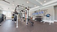 This single-story fitness center is thoughtfully designed to accommodate a wide range of workout styles across several distinct zones. The entry area sets an upscale tone with a warm wood-planked ceiling, herringbone-patterned tile flooring, a granite-topped built-in counter with open storage cubbies, and a wall-mounted mirror. Built-in shelving holds rolled yoga mats, and a water fountain station provides added convenience.

The main strength and functional training area features rubber flooring, a large multi-station power rack with suspension trainers and resistance bands, weight benches, a tiered dumbbell rack, and a punching bag. A bold fitness-themed typographic mural serves as a dynamic focal point on one wall, while large mirrors amplify the sense of space.

The cardio zone is bathed in natural light from oversized windows fitted with white blinds. It houses treadmills, ellipticals, a stair climber, and a recumbent bike, with wall-mounted TVs and ceiling fans overhead.

A dedicated studio room with a tray ceiling and ambient cove lighting offers spin bikes, rowing machines, and yoga mats for group-style or individual sessions. Framed fitness-inspired artwork decorates the walls, completing the polished, motivating atmosphere throughout.