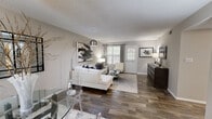 Located in Riverdale, GA, this well-designed 2-bedroom, 2-bathroom single-story home offers a cohesive modern aesthetic throughout. Dark hardwood-style flooring flows seamlessly across the open-concept living and dining area, creating a warm yet contemporary ambiance. The living room is bright and inviting, featuring natural light from multiple windows dressed with plantation shutters and patterned drapes, a textured ceiling, and a ceiling fan that adds both style and comfort. The adjoining dining space provides a natural gathering area that connects effortlessly to the rest of the home. The galley-style kitchen is thoughtfully laid out with rich dark cabinetry, black appliances, tile backsplash, and a window that brings in natural light — offering ample storage and counter space for everyday cooking. The spacious primary bedroom features a generous closet, wood-style flooring, and large windows, while the second bedroom is equally comfortable. Both bathrooms are finished with dark vanity cabinetry, updated fixtures, and wood-style flooring, maintaining the home's consistent design language. A central hallway connects all rooms efficiently, and the overall neutral gray palette throughout creates a clean, modern, and move-in-ready atmosphere.