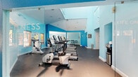 Located at 675 Jamestown Blvd in Altamonte Springs, FL, this fitness center offers a well-appointed, single-floor facility designed to support a comprehensive workout experience. The space is divided into two distinct areas, each serving a specific function within the overall layout.

The main workout area is generously sized, featuring soaring ceilings with elevated clerestory windows that allow natural light to flood the space. Vibrant sky-blue walls create an energizing atmosphere, complemented by durable rubber flooring suited for high-traffic exercise use. The room is outfitted with a full row of TRUE-brand treadmills, elliptical machines, and stationary bikes, as well as a dumbbell rack and weight bench. Large mirrors line portions of the walls, enhancing the sense of openness and allowing users to monitor their form.

The secondary room offers a versatile open-floor space with light hardwood-style flooring and a ceiling fan overhead. Multiple large windows frame direct views of the outdoor pool area and surrounding tropical landscaping, creating a bright and inviting environment ideal for stretching, yoga, or group fitness activities. A painted brick accent wall adds a distinctive architectural touch.

Together, these two rooms form a cohesive and functional fitness facility that balances dedicated cardio and strength training with flexible open space.