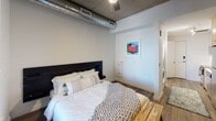 Located in Denver's vibrant RiNo neighborhood, Guest Suite 319 at Walnut Street delivers a thoughtfully designed, single-floor living space that blends modern finishes with industrial character. The open layout makes efficient use of every square foot, connecting the kitchen, living, and sleeping areas in a seamless flow. The kitchen is well-appointed with stainless steel appliances, including an electric range, over-the-range microwave, and dishwasher, all framed by two-tone cabinetry — crisp white upper cabinets contrasting with warm wood-toned lower drawers — and a classic white subway tile backsplash with light quartz countertops. A stacked washer and dryer unit is conveniently integrated into the hallway, adding full in-unit laundry functionality. The sleeping area is anchored by a bold black platform bed and features exposed concrete ceilings with visible industrial ductwork and a ceiling fan, giving the space an authentic urban loft aesthetic. Dark hardwood-style flooring runs throughout, adding warmth and continuity. A window allows natural light to filter into the bedroom. The bathroom offers a clean, minimalist design with a glass-enclosed shower, white tile surround, and matte black fixtures and hardware. Overall, the suite strikes a confident balance between modern convenience and industrial-chic design.