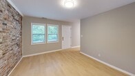 Located at 705 Buck Jones Rd in Raleigh, NC, this single-floor 2-bedroom, 1-bathroom home offers a well-planned layout with a cohesive, updated aesthetic throughout. The living room serves as the focal point of the home, distinguished by a striking full-length exposed brick accent wall that adds warmth and character. Light hardwood flooring runs throughout the entire space, complementing the neutral gray wall tones and white trim for a clean, modern look. Natural light flows in through multiple windows framed by slatted blinds, offering views of the surrounding greenery.

The kitchen is thoughtfully appointed with crisp white shaker cabinetry, granite countertops, a white subway tile backsplash, and a full suite of stainless steel appliances including a range, over-the-range microwave, and dishwasher. The primary bedroom benefits from the same exposed brick feature wall and a window with an outdoor view, creating a cozy yet stylish retreat. The second bedroom is a comfortable, well-lit room with a built-in closet for ample storage. The bathroom includes a full tub/shower combination with white tile surround and a window for natural ventilation. A connecting hallway ties all rooms together in this efficiently designed home.