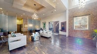 This expansive amenity center is designed to impress, offering a thoughtfully curated mix of social, professional, and recreational spaces across a single floor. The grand lobby welcomes visitors with soaring ceilings, large-format slate-look tile flooring, a dramatic stacked-stone accent wall, and an eye-catching sculptural chandelier that anchors the room. Comfortable lounge seating areas with contemporary furnishings are arranged throughout, bathed in natural light from oversized windows and glass entry doors. A dedicated conference room features floor-to-ceiling windows overlooking a lush outdoor courtyard, a substantial oval conference table with executive leather seating, and a bold wood-and-metal pendant light fixture. The clubhouse lounge and bar area boasts soaring double-height ceilings, industrial-style pendant lighting, a sleek extended counter with bar seating, built-in televisions, and a dark tile backsplash, creating an inviting social atmosphere. The fully equipped fitness center offers a wide selection of strength and cardio machines beneath high ceilings with exposed wood beam accents and vibrant color-blocked walls. A resort-style outdoor pool with umbrella-shaded lounging areas and mature tree landscaping completes this exceptional amenity offering.