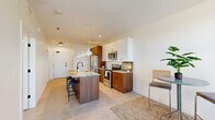 Located at 1405 Rivard Street in Detroit, MI, this modern one-bedroom, one-bathroom unit offers a thoughtfully designed open-concept layout that maximizes its efficient footprint. The combined kitchen and dining area serves as the heart of the space, anchored by a stunning center island topped with granite and fitted with an integrated sink and bar seating—perfect for casual dining or entertaining. The kitchen features a two-tone cabinetry design pairing warm walnut-toned lower cabinets with crisp white upper cabinets, complemented by stainless steel appliances including a French door refrigerator, range, and microwave. Pendant lighting over the island adds a modern, polished touch, while light-toned flooring throughout creates a cohesive and airy feel. The bedroom is generously proportioned, bathed in natural light through a large picture window that frames views of the surrounding neighborhood. Multiple closets provide ample storage throughout the unit. The full bathroom is sleek and contemporary, featuring a frameless sliding glass shower enclosure with black hardware accents, a wood-toned vanity with granite countertop, and clean neutral finishes. An in-unit laundry area adds everyday convenience. The overall ambiance is clean, modern, and well-appointed, reflecting a fresh and functional urban living environment.