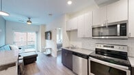 Located at 300 W State St in West Lafayette, Indiana, this thoughtfully designed unit offers four bedrooms and three bathrooms across a single floor. The open-concept kitchen and living area serves as the heart of the space, featuring stainless steel appliances — including a range, microwave, and dishwasher — paired with two-tone cabinetry in white and dark wood finishes, a white subway tile backsplash, and a stainless steel sink. Wood-style flooring runs throughout, adding warmth and visual continuity. The living area is bright and welcoming, with a sliding glass door that opens onto a private balcony, providing outdoor views and natural light. Each bedroom is efficiently designed with ceiling fans and windows that bring in daylight. The primary bedroom includes a dedicated walk-in closet fitted with built-in shelving and a dresser. The bathrooms are finished with classic penny-tile flooring, subway tile shower surrounds, dark-toned vanities, and framed mirrors, offering a clean and contemporary aesthetic. The overall design balances modern finishes with functional layouts, making this a well-appointed unit ideal for shared living in the heart of West Lafayette.