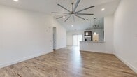 This well-appointed single-story home in Opelika, Alabama offers a thoughtfully designed open-concept layout across three bedrooms and two bathrooms. The combined living room and kitchen area serves as the heart of the home, highlighted by soaring vaulted ceilings and a dramatic oversized ceiling fan that enhances the sense of spaciousness. Warm hardwood-style flooring flows throughout the main living areas, complemented by crisp white walls and abundant natural light. The kitchen features sleek gray cabinetry, stainless steel appliances including a French door refrigerator, a microwave, and a range, alongside a peninsula with light stone countertops and pendant lighting — ideal for casual dining or entertaining. A sliding door off the kitchen provides access to the outdoors. The bedrooms offer plush carpeting and ample closet space, with the primary bedroom featuring a generously sized walk-in style closet. The bathrooms are finished with striking marbled tile flooring and full tub-shower surrounds, dark stone vanity countertops, and modern cabinetry. A dedicated laundry room with wire shelving and tiled flooring adds practical convenience. The entry area features vaulted ceilings and a ceiling fan, setting a welcoming tone throughout this clean, contemporary home.