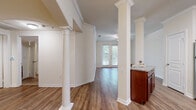 This single-floor residence showcases a thoughtful layout with refined architectural details throughout. The open living and dining area is defined by striking decorative columns with classical capitals and crown molding, lending an air of elegance to the space. Warm hardwood-style flooring flows seamlessly through the main living areas, complementing the neutral, light-toned walls that create a bright and welcoming atmosphere. French doors invite natural light into the living area and provide views of the surrounding greenery, while a ceiling fan adds both function and style.

The kitchen is well-appointed with rich cherry wood cabinetry, granite countertops, a subway tile backsplash, and a full suite of stainless steel appliances including a refrigerator, dishwasher, range, and microwave. A built-in wine rack adds a distinctive touch to the cabinetry design. A peninsula counter provides additional prep space and connects the kitchen to the main living area.

Bedrooms feature plush carpeting, ceiling fans, and arched architectural accents, with generous natural light from exterior-facing windows. The primary bathroom is well-equipped with a granite vanity, a glass-enclosed stand-up shower with tile detailing, a soaking tub, and hardwood-style flooring, offering a clean and functional retreat.