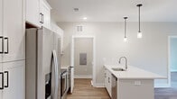 Located at 1425 Aversboro Rd in Garner, NC, this single-floor home offers a clean, modern aesthetic throughout. The open-concept kitchen is a standout feature, showcasing white shaker-style cabinetry with matte black hardware, stainless steel appliances including a French door refrigerator and range, and a center island with a white quartz countertop, undermount sink, and stylish pendant lighting overhead. Light wood-tone luxury vinyl plank flooring flows seamlessly throughout the home, providing both durability and visual continuity. The living area is bright and airy, featuring a ceiling fan and a large picture window with transom detail that frames views of surrounding trees. A glass door opens directly to a private outdoor deck with black metal railing, extending the living space outdoors. Bedrooms are well-proportioned, each finished with LVP flooring, ceiling fans, and generous windows that invite natural light and wooded views. A walk-in closet with wire shelving systems provides ample organized storage. The bathroom includes a soaking tub, toilet, and grab bars, finished in a clean, neutral palette. A dedicated laundry room houses a full-size Whirlpool washer and dryer with overhead wire shelving. The home's consistent use of neutral tones, modern fixtures, and quality finishes creates a cohesive and inviting living environment.