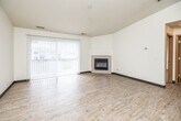 This single-floor unit offers a practical and functional layout spread across several distinct areas. The living room serves as the focal point of the space, showcasing light wood-style flooring, a textured ceiling, and a corner fireplace with a clean, tile-surround design. A large vertical-blind-covered sliding glass door floods the room with natural light, creating a bright and open atmosphere.

The kitchen is efficiently arranged in an L-shaped configuration, featuring warm oak cabinetry extending to the upper walls for ample storage, dark laminate countertops, and white appliances including an electric range, over-the-range microwave, and refrigerator. The kitchen flows directly from the main living and dining area, reinforcing the open-concept feel of the unit.

The bedrooms are carpeted in neutral tones and include generous closet space with built-in shelving and bi-fold oak doors. Each room is well-proportioned, providing comfortable accommodation. The bathroom is cleanly finished with light wood-look flooring, a full tub-shower combination, a toilet, and a wood-fronted vanity with a light countertop. Throughout the unit, consistent oak-toned doors and trim details provide a cohesive, understated character.
