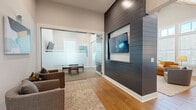 Located at 40 Hathaway Ln in Lebanon, TN, this thoughtfully designed single-floor space combines modern aesthetics with functional versatility. The layout includes a welcoming living area and a connecting hallway that flows seamlessly between zones.

The living room is an immediate standout, boasting soaring vaulted ceilings clad in warm wood paneling and an abundance of natural light pouring in through large, multi-pane windows. The crisp white walls are complemented by warm-toned hardwood flooring that runs throughout the space, creating a cohesive and inviting atmosphere. A bold dark shiplap accent wall serves as the centerpiece, featuring a recessed, wall-mounted display and built-in white cabinetry below.

A glass-enclosed room with frosted panel accents and sliding glass doors offers a semi-private area suited for meetings or focused work, furnished with a mid-century style table and chairs. This transparent partition allows light to pass freely while maintaining a sense of separation.

The hallway connects the areas with ease, decorated with contemporary abstract artwork that adds color and character. Throughout the space, the design strikes a balance between modern and mid-century influences, with curated furnishings, warm textures, and an overall ambiance that is both professional and welcoming.