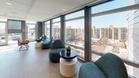 Located at 222 M St SW in Washington, DC, this contemporary amenity lounge offers a sophisticated and well-appointed gathering space designed for both relaxation and socializing. The single-level layout is thoughtfully organized into distinct zones, each offering a unique experience while maintaining a cohesive modern aesthetic throughout.

Large-format tile flooring anchors the interior, complementing the clean lines and neutral palette of the space. One of the most striking features is the expansive floor-to-ceiling window wall, which floods the lounge with abundant natural light and frames panoramic views of the surrounding Washington, DC skyline. Clusters of rounded, teal upholstered lounge chairs and low-profile accent tables are arranged to take full advantage of these views, creating inviting conversation areas with a relaxed, contemporary feel.

A wet bar area serves as a functional centerpiece, featuring warm wood cabinetry, a white countertop with an integrated sink, under-counter refrigeration units, and a horizontally slatted wood accent wall with mounted flat-screen displays — lending a refined, residential quality to the space.

Glass doors provide direct access to an outdoor terrace, where additional seating and open-air amenities extend the lounge experience. Colorful artwork punctuates the walls throughout, adding visual interest and character to this polished, light-filled retreat.