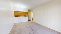 Located at 555 E Limberlost Dr in Tucson, Arizona, this one-bedroom, one-bathroom unit offers a functional and efficient single-floor layout. The combined living and kitchen area forms the heart of the home, with soft carpeting underfoot and a modern drum pendant light that anchors the space. A sliding glass door with vertical blinds provides direct access to a private patio, allowing natural light to flow in. The kitchen is designed in a galley style, featuring warm wood cabinetry, light stone-patterned countertops, and durable wood-look flooring. Appliances include an electric range and dishwasher, with ample upper and lower cabinet storage lining both sides of the kitchen. A pass-through counter visually connects the kitchen to the living area. The bedroom is a comfortable retreat with plush carpeting, a bright window with views of the surrounding landscape, and direct access to both the bathroom and a dedicated closet. The bathroom is well-appointed with a full tub-shower combo, a wood-vanity with a stone-top, and wood-look flooring that complements the rest of the home. Textured ceilings throughout add a classic touch to this clean, move-in-ready Tucson residence.