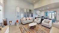 Located in Estero, Florida, this single-floor community clubhouse on Everblades Parkway North offers a thoughtfully designed, open-concept space that seamlessly blends comfort and functionality. The grand lounge area serves as the heart of the space, anchored by a dramatic floor-to-ceiling natural stone fireplace with a wall-mounted flat-screen television above. Soaring ceilings amplify the sense of openness, while an abundance of windows dressed with clean white blinds flood the interior with natural light. Light wood-tone flooring runs throughout, contributing to the bright, welcoming ambiance. Elegant chandeliers add a refined touch overhead. The lounge is furnished with comfortable neutral-toned seating arrangements centered on a vibrant, multicolored area rug, complemented by a curated gallery of large-scale framed artwork along the walls. A reception area near the entrance features a curved blue accent desk with granite countertops, providing a professional and inviting welcome point. The fully equipped kitchen showcases rich dark cabinetry, granite countertops, stainless steel appliances, and a curved island with bar seating beneath pendant lights — ideal for community gatherings and events. Altogether, the space delivers a polished, resort-inspired atmosphere suited for socializing and community engagement.