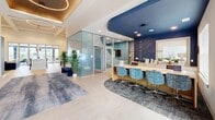 The Viridian Apartments clubhouse at 389 Plano Rd in Bowling Green, Kentucky is a thoughtfully designed, single-floor amenity facility spanning an expansive footprint. The space is anchored by a stylish leasing lobby, where a bold navy curved ceiling accent, slatted wood wall panels, and frosted glass-walled private offices create a polished, contemporary first impression. A long service counter with blue upholstered chairs and branded signage reinforces the professional atmosphere.

Adjacent to the lobby is a spacious lounge area with soaring coffered ceilings, large floor-to-ceiling windows, and direct access to an outdoor patio. A linear gas fireplace with a white shiplap surround and a wall-mounted flat-screen TV serves as the focal point, complemented by a sectional sofa, accent chairs, and a geometric area rug. A self-serve refreshment station adds everyday convenience.

The fitness wing is extensive and well-equipped, featuring a strength and free weights area with a retractable garage door that opens to the outdoors, a cardio floor with treadmills, ellipticals, and stair climbers set against vibrant yellow and charcoal accent walls, and a dedicated spin and rowing studio with floor-to-ceiling mirrors and individual screens.

A private wellness pod room houses a high-tech relaxation chair for recovery. The game lounge rounds out the amenity offering with a pool table, shuffleboard, arcade games, and a virtual golf simulator beneath pendant lighting and bold geometric wall graphics.