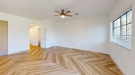 This two-story home in Royal Palm Beach, Florida offers six bedrooms and three bathrooms across two well-proportioned floors, making it an ideal choice for large households. Throughout the home, striking herringbone-patterned hardwood flooring creates a cohesive and stylish aesthetic that flows from room to room.

The main floor features an open-concept kitchen and living area. The kitchen is equipped with stainless steel appliances, two-tone cabinetry combining white upper cabinets with warm wood lower units, a white countertop island with pendant globe lighting, and track lighting overhead. The space opens seamlessly to the living area.

The six bedrooms are bright and airy, each featuring the signature herringbone flooring, ceiling fans with light fixtures, and windows with blinds that frame views of the surrounding greenery. The generously sized primary bedroom offers ample space and comfort. Two closets serve the home, including a walk-in style with wire shelving systems for organized storage.

The three bathrooms are clean and modern, with one featuring a glass-enclosed walk-in shower adorned with large-format horizontal tile and chrome fixtures. A dedicated garage with an automatic opener and electrical panel provides convenient parking and utility access. Outside, a landscaped backyard with mature trees completes this well-appointed home.
