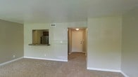 This 2-floor residence offers a straightforward and functional layout designed for comfortable everyday living. The main living area is finished with wall-to-wall carpeting in a neutral tone, creating a warm and cohesive feel throughout the space. A pass-through opening connects the living area to the kitchen, allowing for easy interaction between the two spaces. The kitchen features dark cabinetry, a stainless steel refrigerator, and a granite or stone-style countertop visible through the pass-through, adding a touch of contrast to the otherwise light interior.

The entryway is clearly defined, with a white front door and a ceiling-mounted light fixture that provides a welcoming transition into the main living space. Walls throughout are finished in a soft, neutral tone, contributing to a clean and understated aesthetic. A ceiling-mounted HVAC vent is visible, indicating a central air system. White baseboards frame the carpeted floors, adding a crisp finishing detail. The overall ambiance is calm and move-in ready, with the two-floor layout offering additional living or sleeping space above the main level.